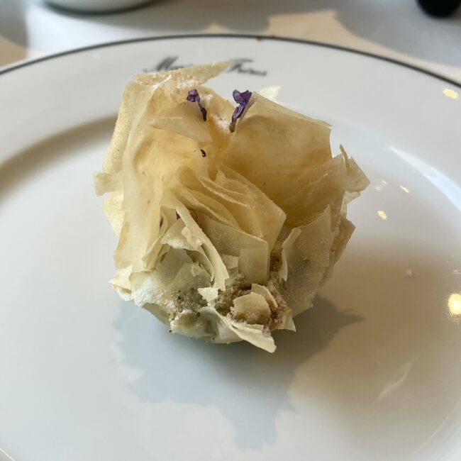 マリアージュフレールのスイーツ「青茶 ‘ノエル インペリアル’ 香るクルスタッド」。薄いパートフィロ生地が幾重にも重なり、花のように美しい造形。中にはマロングラッセが包まれており、トップには紫色のエディブルフラワーが飾られている。