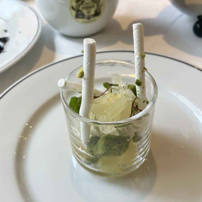 マリアージュフレールのグラスデザート「緑茶 ‘ノエル プリンシエ’ 輝く文旦のヴェリーヌ」。透明なグラスの中に、フレッシュな文旦の果肉、抹茶のスポンジやクリーム、ピスタチオが層になり、白いメレンゲの棒が飾られた美しいパフェ仕立て。