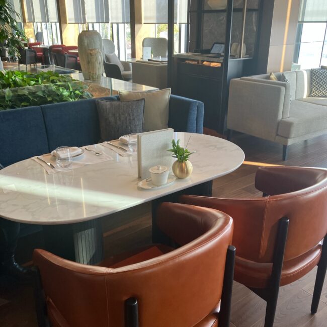 フェアモント東京「Vue Mer」のボックスソファ席。深いブルーのソファと大理石調のテーブル、落ち着いたオレンジのレザーチェアが配置された、ゆとりある座席。