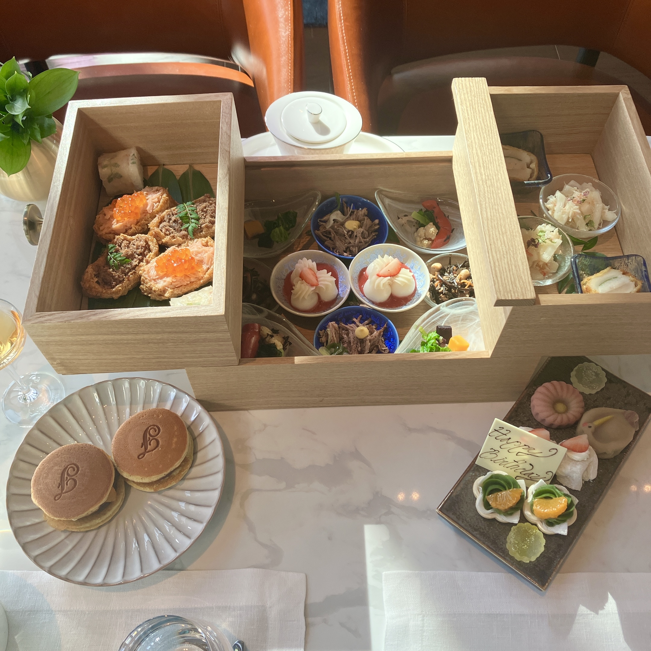 フェアモント東京「Vue Mer」の和アフタヌーンティー。木箱に入ったセイボリー、焼きたてどら焼き、和菓子、誕生日プレートがテーブルいっぱいに並んでいる様子。