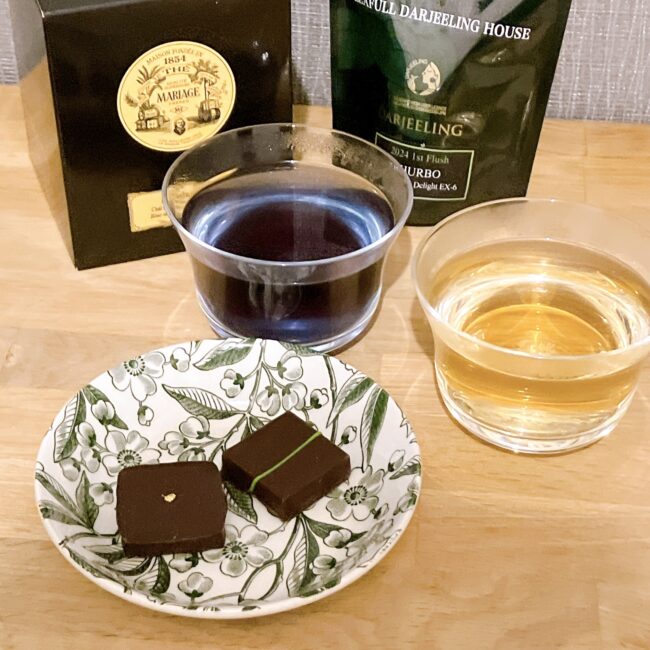イナムラショウゾウのショコラと紅茶のペアリング検証風景。金箔のカカオと緑の線の抹茶ショコラ、背後にリーフルダージリンハウス「タルボ・ファーストフラッシュ」とマリアージュフレール「チャイワラ」のパッケージと茶液