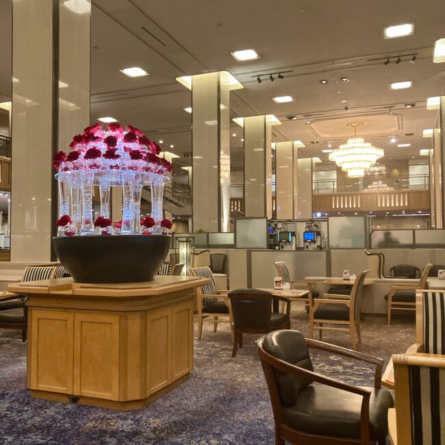 帝国ホテル 東京本館1階「ランデブーラウンジ」の内観。高い天井、奥に見える巨大なシャンデリア「ゴールデンローズ」、手前の赤いバラの装飾が、重厚でクラシックな雰囲気を醸し出している。