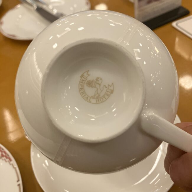 帝国ホテルのティーカップの裏面。金色の「舵輪とライオン」のロゴマーク（バックスタンプ）が刻印されている。