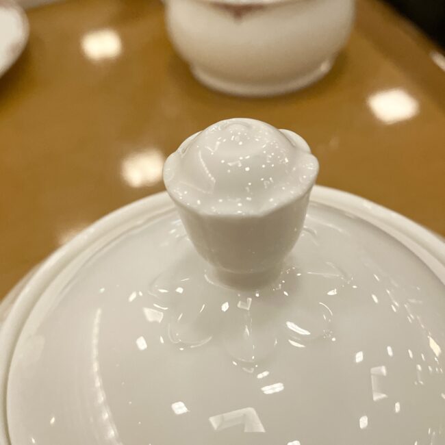 帝国ホテルの白いティーポットの蓋のアップ。持ち手（つまみ）の部分が、薔薇の蕾のような花のモチーフになっている。