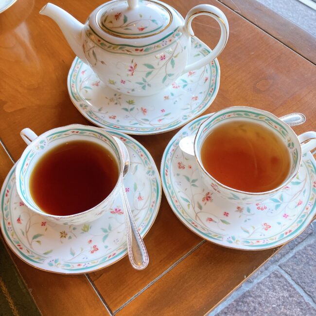 ホテル椿山荘東京「ル・ジャルダン」のアフタヌーンティー。窓際の木製テーブルに、ノリタケの洋食器「花更紗（はなさらさ）」シリーズのティーポットと、2種類の異なるクラシックティーが注がれた様子。