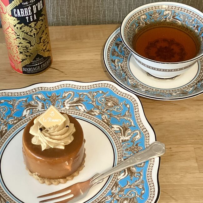 マリアージュフレールの紅茶「カレ ドール (CARRE D'OR)」の缶、Wedgwood（ウェッジウッド）フロレンティーン ターコイズの食器に入った紅茶、ル・ポミエの塩キャラメルムースケーキが並んだペアリング写真。"
