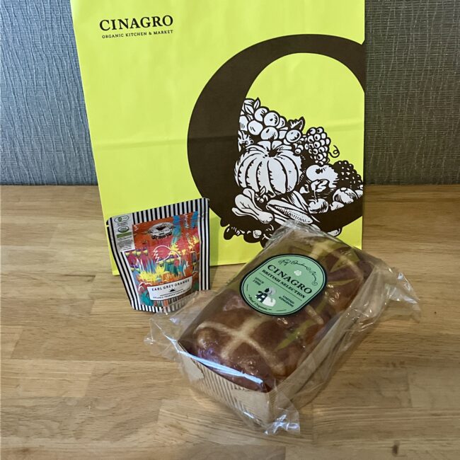 CINAGRO（シナグロ）の鮮やかな黄色のショッパーバッグと、購入したオーガニックのアールグレイオレンジ紅茶、そしてローフ型の大きなホットクロスバンズ。