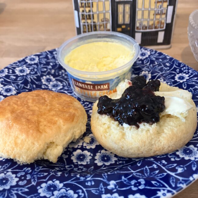 ファーラーズのスコーンとランゲージファームのクロテッドクリーム。ファーラーズのブルーの食器に、半分に割ったスコーンがあり、ロダスのクロテッドクリームとブルーベリージャムがたっぷりのせられている。奥にファーラーズの紅茶缶（店舗の絵柄）が見える。