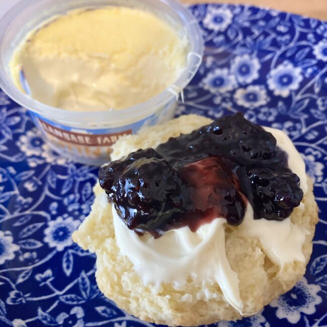 ブルーの美しい柄のお皿に乗ったファーラーズのスコーン。半分に割った生地の上に、ランゲージファームのクロテッドクリームとダークチェリー系のジャムがたっぷりと乗っている。