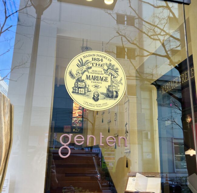 entenのガラスの入り口ドアのアップ。ガラスにはマリアージュフレールのゴールドの大きな円形ロゴマークが貼られており、その下に「genten」のロゴが見える。