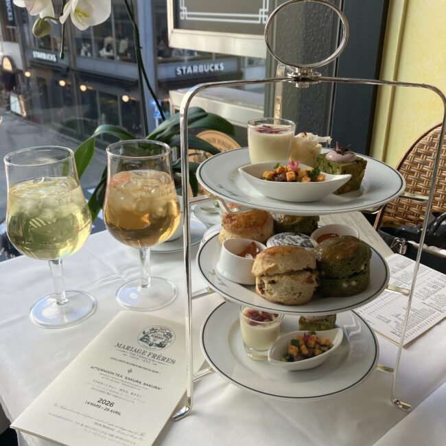 マリアージュフレール銀座松屋通り店のアフタヌーンティー「サクラ、サクラ! 2026」の3段シルバーティースタンド。上段のセイボリー、中段の焼き立てスコーン(抹茶含む)、下段のスイーツが美しく並び、手前には2種類のアイスティーとメニューが添えられている。