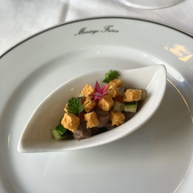 緑茶‘ヴェール プロヴァンス’に彩られた仔羊とズッキーニのタルタル。舟形の白い皿に乗っており、鮮やかな花とクルトンがトッピングされている