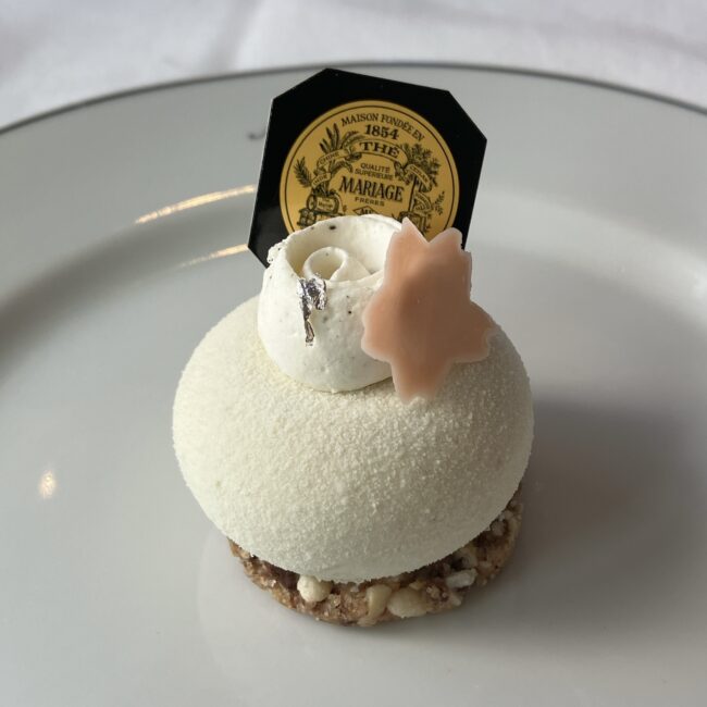 マリアージュフレールの緑茶‘サクラ 2026’を使用したムースケーキ。白い球体のムースに、桜の花びらのチョコとマリアージュフレールのロゴピックが乗っている。