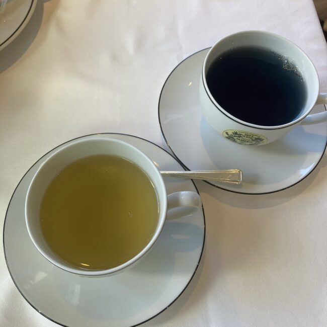 マリアージュフレールのティーカップに注がれた2種類のホットティー。手前は淡い黄色のグリーンティーベースのサクラ2026、奥は深い青色の青茶ベースのサクラブルー。水色の対比。