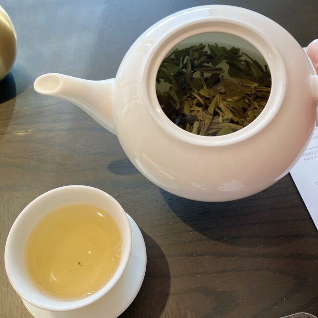 ジャヌ東京「虎景軒」の中国茶。白いティーポットの蓋を開けた様子。中にはティーバッグではなく、大きく開いた本格的な茶葉がたっぷりと入っている。