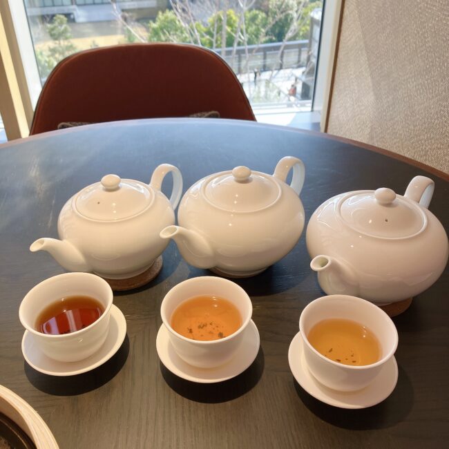 ジャヌ東京「虎景軒」の中華アフタヌーンティーのフリーフロー。3種類の中国茶（プーアール茶、ホワイトティー、ジャスミンティー）が入った白いティーポットとカップが並んでいる。お茶の色味の違いがはっきりとわかる。
