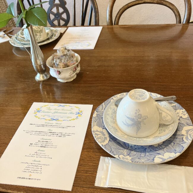 タイニートリアティールームのテーブルセッティング。イースターアフタヌーンティーのメニュー表と、イギリスの伝統的な陶磁器ブランド「バーレイ（Burleigh）」の美しいブルーのティーカップ＆ソーサーが用意されている様子。