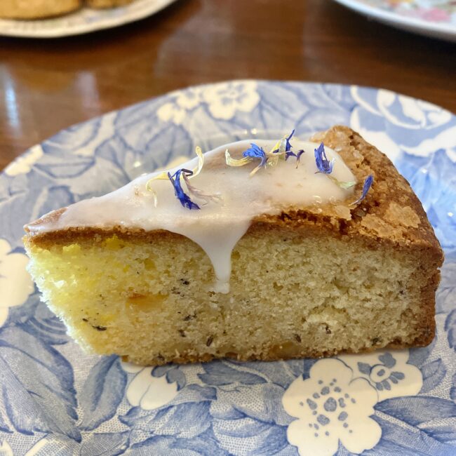 タイニートリアの中段の英国菓子「スプリングシードケーキ」。しっとりとした生地の上に真っ白なアイシングがかけられ、その上に青や黄色の可憐なエディブルフラワー（食用花）が散りばめられている。