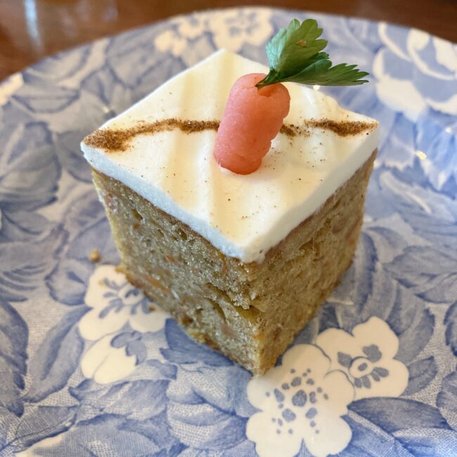 タイニートリアの中段の英国菓子「ココナッツキャロットケーキ」。スパイスの効いた四角いケーキの上に真っ白なクリームが塗られ、さらにその上にちょこんと可愛らしいニンジンのマジパン細工が飾られている。