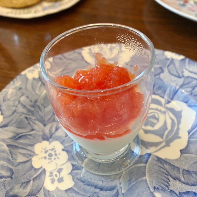 タイニートリアのイースターアフタヌーンティーのスイーツ。小さなグラスに入った「レモンポセット＆ブラッドオレンジジェリー」。白いレモンポセットの上に、鮮やかなオレンジ色のブラッドオレンジジェリーが重ねられている。ブルーの花柄のバーレイの皿の上に乗っている。