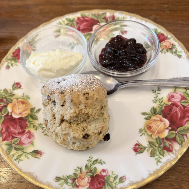 温め直してもらった熱々のイースタービスケットスコーン。華やかな薔薇柄のプレートに、たっぷりのクロテッドクリームとブルーベリージャムが入ったガラスボウルが添えられている。