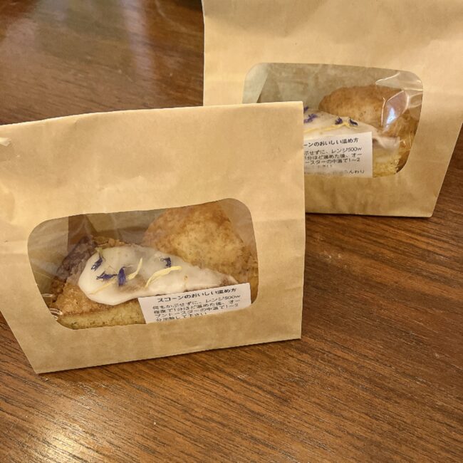 タイニートリアティールームで食べきれなかったスコーンやケーキを持ち帰り用にしていただいた様子。中身が見える窓付きのクラフト袋に丁寧に個包装されており、袋の表面には「スコーンのおいしい温め方（レンジやトースターの時間）」が書かれた親切なシールが貼られている。