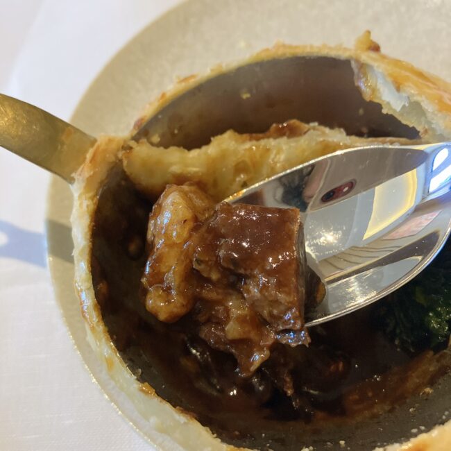 「牛ほほ肉のパイ包み」の中身のアップ写真。スプーンですくわれた、大きくてホロホロに煮込まれた艶やかな牛ほほ肉。