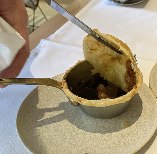 切り開かれたパイの蓋が持ち上げられ、中から湯気とともに濃厚なデミグラスソースのシチューが顔を出した様子。