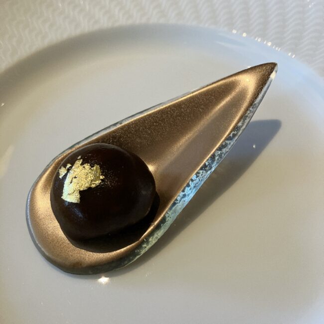 帝国ホテル京都アフタヌーンティーの「鴨肉のリエット」。金箔が飾られた黒い球体のリエットが、ティアドロップ型のモダンなガラススプーンに乗せられている。