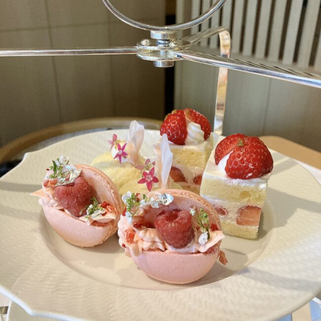 帝国ホテル京都アフタヌーンティーの3段スタンド上段。名物のイチゴのショートケーキや、エディブルフラワーと銀箔が飾られた華やかなラズベリーのマカロンが並ぶ。