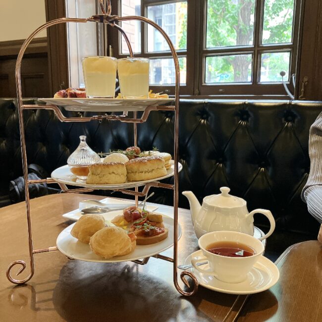 Café 1894のクラシックな3段アフタヌーンティースタンド。手前には白いティーポットと紅茶が美しくセッティングされている。