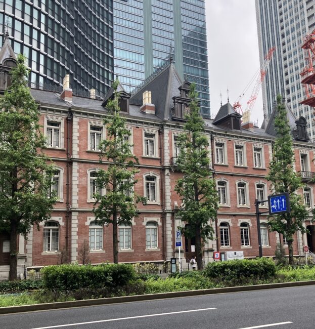 丸の内にある三菱一号館のクラシカルな赤レンガの外観と、背景にそびえる高層ビルのコントラスト。