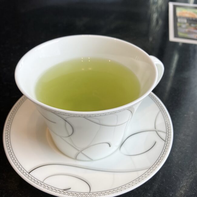 鮮やかな緑色が美しい八女茶のホットティー。シルバーの模様が入った白いティーカップで提供されています。
