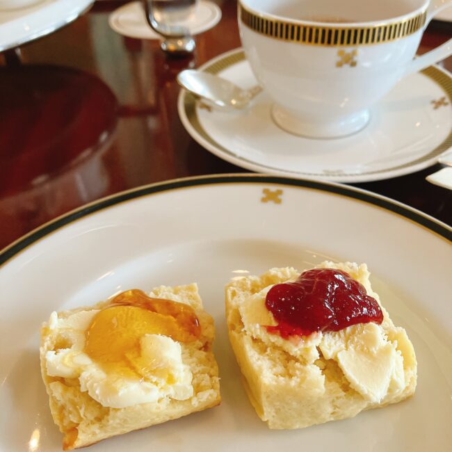 帝国ホテル英国フェアの四角いバッキンガムスコーン。クロテッドクリームといちごジャム、はちみつをたっぷりと乗せたクローズアップ写真"