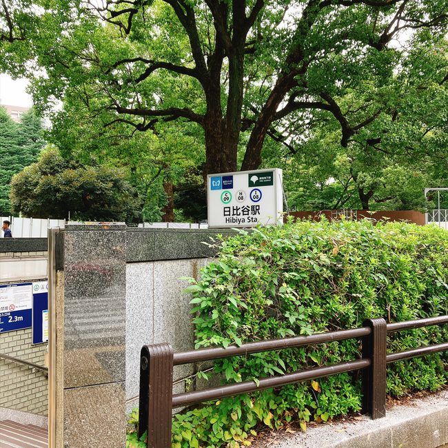 緑豊かな大きな木々に囲まれた東京メトロ日比谷駅の出口看板。日比谷パレスへのアクセスの様子。